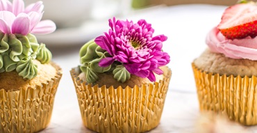 photo of 3 carrot cupcakes in gold wrappers, decorated with green icing and pink flowers