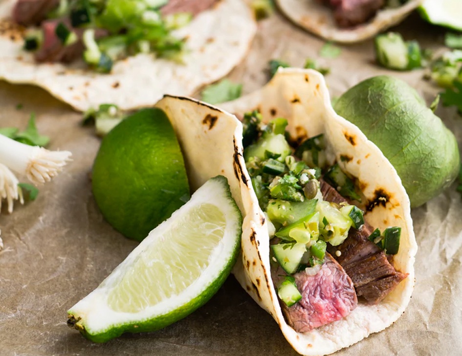 steak taco with avocados, with cut limes on the side